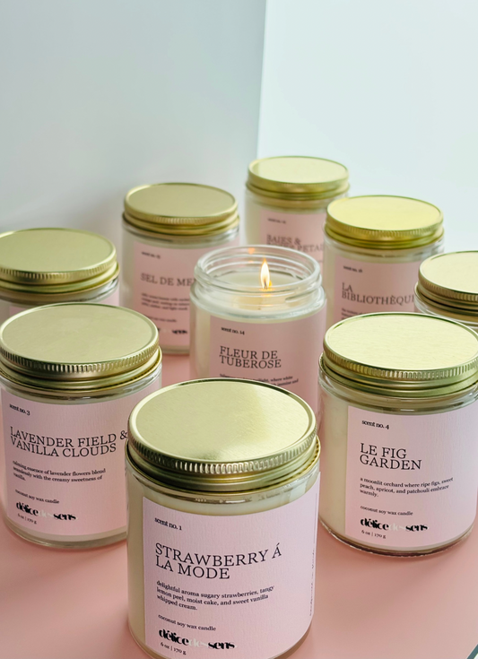 Assorted coconut soy candles by Délice des Sens in glass jars with gold lids, featuring scents including Strawberry à la Mode, Lavender Field & Vanilla Clouds, Le Fig Garden, Fleur de Tuberose, and Sel de Mer